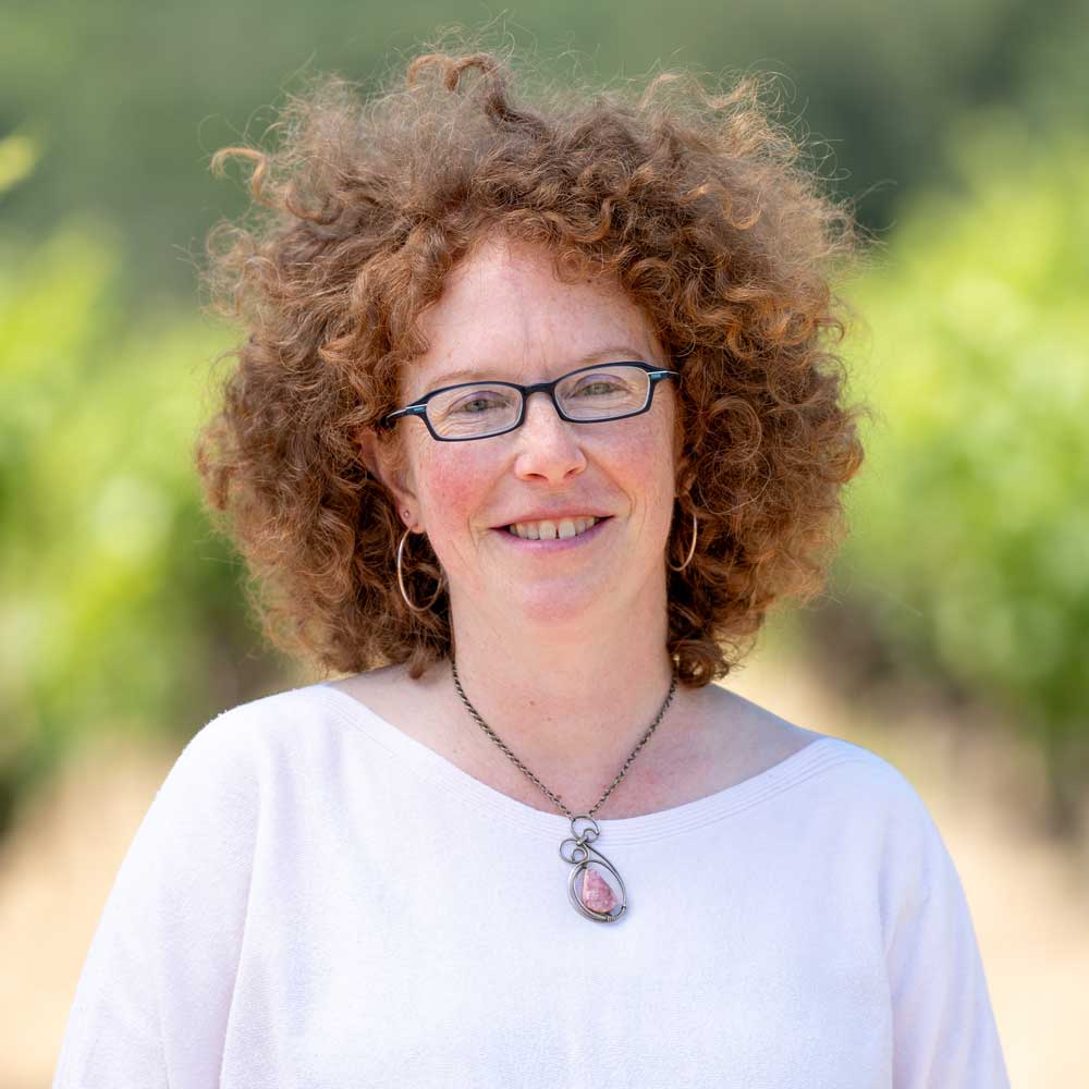 Person with curly red hair wearing glasses and a white shirt outdoors