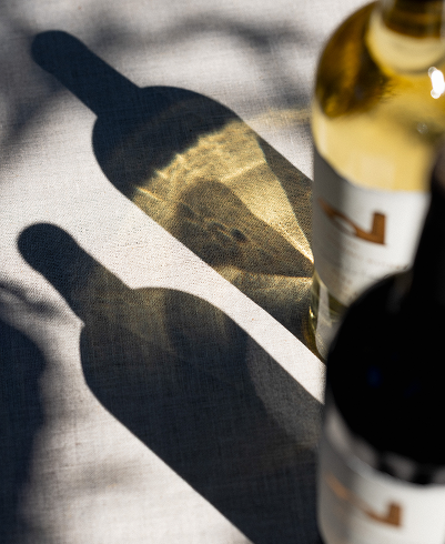 A bottle of red and white wine with shadows reflecting on a light grey surface 