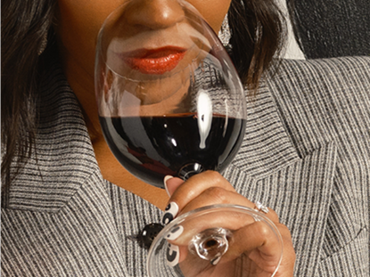 Person holding a wine glass with red wine, wearing a gray blazer.